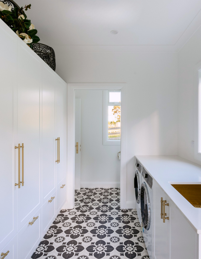 laundry-mudroom-cabinetry-te-puke-bay-of-plenty Laundry and mudroom with full-height white cabinetry, a brass sink and a patterned floor, designed by Design Suite.